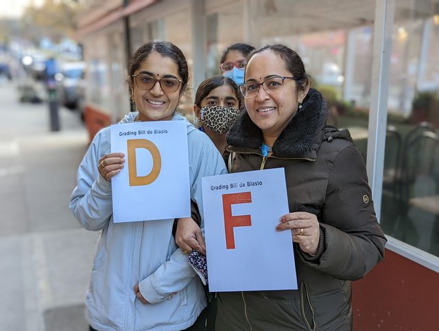 Sruthi Manish on the left and Thara Madathody on the right hold up individual grades assessing Mayor Bill de Blasio's tenure in office: Sruthi holds a "D"